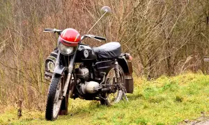 Czarny skuter z czerwonym kaskiem na kierownicy. Rozrusznik kręci ale nie odpala, stoi na trawie wśród gałęzi.