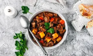 En mustig boeuf bourguignon med möra köttbitar, potatis och morötter i en rik vinbaserad sås. Serveras med en skiva rustikt bröd.