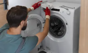 Mężczyzna w czerwonych rękawiczkach wyjmuje szufladę na proszek. Instrukcja jak podłączyć pralkę krok po kroku.