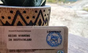Dokument mit "Keine Wohnung in Deutschland" und einem Stempel. Ein Sukkulent in einem Topf steht daneben. So kann man dauerhaft reisend melden.