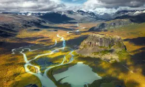 Weites Tal mit Fluss und Berg in Schwedens Nationalparks. Herbstliche Farben und dramatische Wolken über der Landschaft.