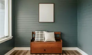Un banc coffre en bois avec coussins, devant un mur de lambris bleu-gris fraîchement peint. Un cadre vide est accroché au-dessus.
