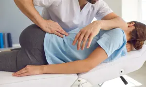 Ein Therapeut behandelt einen Beckenschiefstand. Er legt seine Hände auf den Rücken einer liegenden Person, um eine Korrektur vorzunehmen.