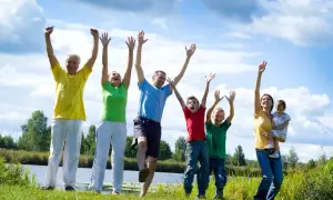 Familia disfrutando de actividades al aire libre, saltando y riendo junto a un lago.