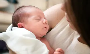 Śpiące, 3-tygodniowe dziecko wtulone w ramiona mamy. Delikatne światło podkreśla jego maleńkie rysy.