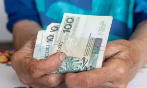 Dłonie trzymają polskie banknoty 100 zł. Czekamy na informacje, kiedy będzie wypłacana trzynastka.