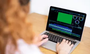 Osoba pracuje na laptopie, edytując wideo. Na ekranie widać zielony podgląd i oś czasu, co sugeruje, że uczy się, jak nagrywać ekran na laptopie.