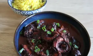 Un plat de daube de poulpe savoureux, garni de ciboule fraîche, servi avec du riz jaune parfumé.
