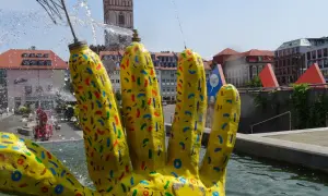 Żółta, kolorowa dłoń fontanny w centrum Frankfurtu nad Odrą, z widoczną wieżą kościelną w tle.