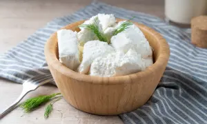 Półmisek z twarogiem półtłustym, udekorowany koperkiem. Obok widelec i szklanka mleka. Idealny na lekki posiłek, z niską zawartością kcal.