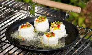 Vier runde Ziegenkäse auf einer Grillpfanne mit geschmolzenem Käse und Paprikastückchen. Perfekt für vegetarische Grillrezepte einfach.