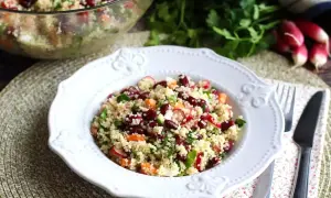 En härlig couscous sallad med bönor, morötter och rädisor, serverad på en vit tallrik.