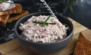 Un bol de rillettes de thon crémeuses, garnies de ciboulette, prêtes à être tartinées sur du pain grillé.