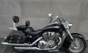 Czarny motocykl Honda VTX 1800 Neo z sakwami i oparciem dla pasażera, lśniący chromem na tle szarej ściany.