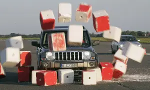 Jeep rast durch rote und weiße Blöcke, die durch die Luft fliegen. Die Szene illustriert die **Bremsweg Formel** in Aktion.