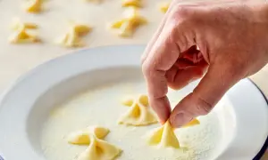 Hand formt frische Farfalle für leckere Farfalle Rezepte. Viele kleine Nudelschmetterlinge liegen bereit.