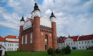 Ceglana cerkiew z kopułami i krzyżem, przypominająca o historii **unii brzeskiej**. Obok białe budynki klasztorne.