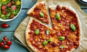 En saftig vegetarisk pizza med tomatsås och ost, toppad med färsk basilika. Bredvid en fräsch sallad med gröna bönor och körsbärstomater.