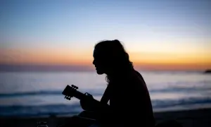 Sylwetka grającej na ukulele osoby na tle zachodzącego słońca nad morzem. Gdzie ta keja chwyty?