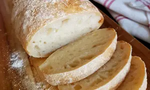 Frisch gebackenes ciabatta brot mit knuspriger Kruste und luftiger Krume, auf einem Holzbrett mit etwas Mehl bestäubt.