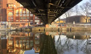 Pod mostem w Berlinie odbija się w rzece ceglana architektura i nagie drzewa.