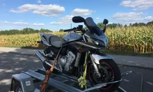 Srebrny motocykl Yamaha na przyczepce, na tle pola kukurydzy i błękitnego nieba z chmurami.