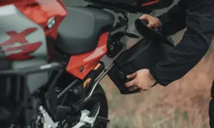 Mężczyzna montuje czarną sakwę motocyklową do czerwonego motocykla.