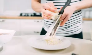Kobieta w paski ściera ser na tarce na talerz.