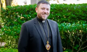 Uśmiechnięty mężczyzna w czarnym garniturze i z krzyżem na szyi, być może najmłodszy kardynał.