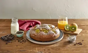 Torta kiwi e cioccolato cosparsa di zucchero a velo, con kiwi freschi, gocce di cioccolato, latte e succo d'arancia su un tavolo di legno.