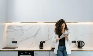 Donna con tablet in cucina moderna, valuta quanto costa rifare una cucina con finiture in marmo e illuminazione a led.