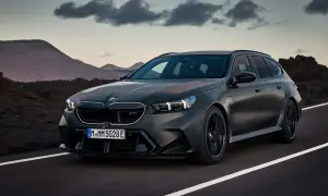 Mroczny, matowy BMW M5 Touring pędzi po pustej drodze, z górami w tle.