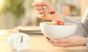 Une personne mange des céréales avec des fraises, une horloge à côté. Le jeûne intermittent avant après 1 mois, une nouvelle habitude alimentaire.