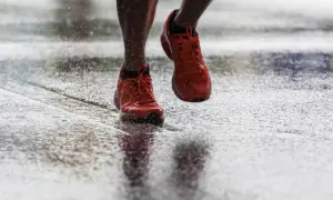 Scarpe da corsa arancioni che schizzano sull'asfalto bagnato, un'immagine di determinazione nel correre sotto la pioggia.