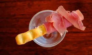Ein knuspriger Grissini mit zartem Schinken, serviert in einem Glas.