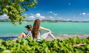 Dzieci siedzą plecami do widza, patrząc na turkusowe wody Balatonu na Węgrzech.