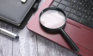 Lupa na laptopie, obok notatnika i długopisu. Szukam numeru seryjnego laptopa, by go zidentyfikować.