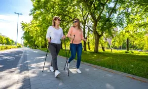 Deux femmes font de la marche nordique dans un parc ensoleillé, une activité idéale pour perdre du poids en marchant.