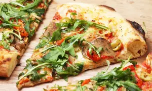 Kawałki pizzy z rukolą, oliwkami i warzywami na drewnianym tle.