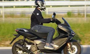 Osoba w kasku i kurtce jedzie na czarnym skuterze Keeway po drodze.