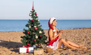 Kobieta w stroju Mikołaja pije koktajl na plaży obok choinki. Czy 28 grudnia jest dniem wolnym od pracy?