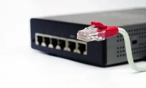 Czerwony wtyk kabla sieci ethernet podłączony do czarnego switcha z wieloma portami.