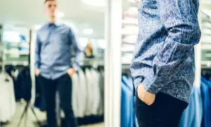 Mann im Spiegel prüft seinen lässigen kleidungsstil herren. Blaues Hemd mit Muster, schwarze Hose.