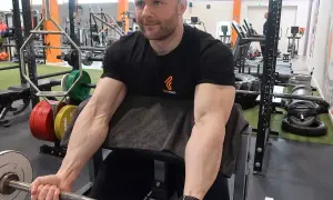 Mann trainiert Bizeps mit Langhantel im Fitnessstudio. Deutlich sichtbare Muskeln beim Bizeps dehnen.