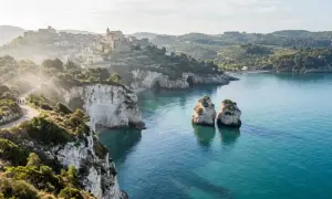 Panoramica mozzafiato del Gargano, Puglia, con scogliere bianche, mare cristallino, faraglioni e un borgo arroccato.