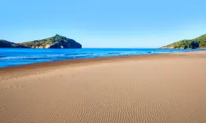 Piękna plaża w Sarigerme, z piaszczystym brzegiem i turkusowym morzem, w tle skaliste wzgórza.