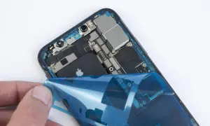 Dłoń odkleja niebieską folię od wnętrza iPhone'a XR z widoczną baterią.