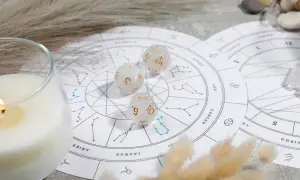 Karty zodiaku, kostki z symbolami planet i płonąca świeca tworzą mistyczną atmosferę.