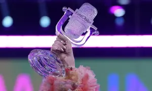 Ręka trzyma kryształowy mikrofon z logo Eurowizji, symbol zwycięstwa i historii konkursu.