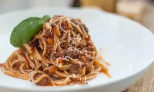 Pyszne spaghetti bolognese z parmezanem i listkiem bazylii na białym talerzu.